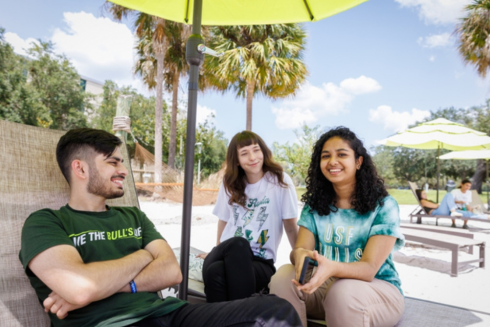 Three students sitting on ֱ's beach on the Tampa campus, linking out to Why ֱ webpage.